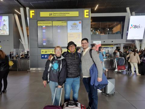 Tres personas sonrientes posan en un aeropuerto con maletas.