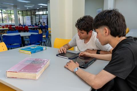 Dos jóvenes estudiantes se reúnen en una mesa de estudio para usar una tablet y repasar materiales de aprendizaje.