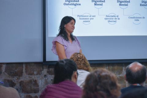 Una mujer está presentando frente a una pantalla con información sobre la dignidad humana.