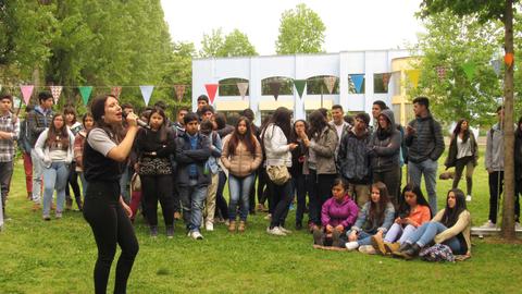 Una joven canta frente a un grupo de espectadores en un evento al aire libre.