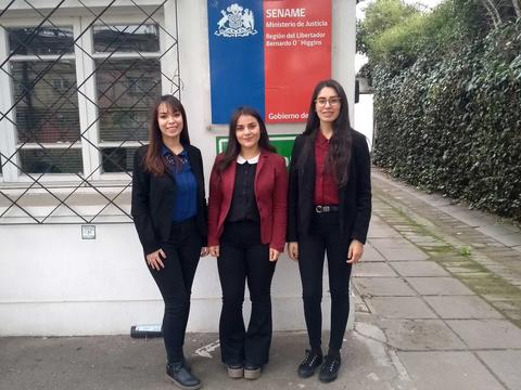 Tres mujeres vestidas formalmente posan frente a un edificio gubernamental.