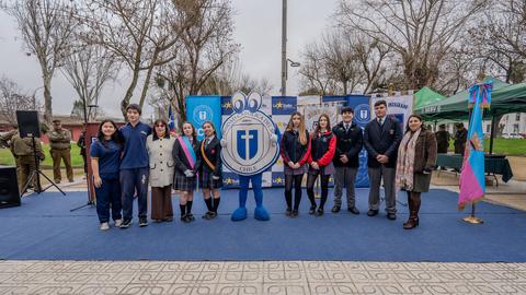 Un grupo de estudiantes y profesores participa en una actividad en un parque, con un personaje animado como mascota.