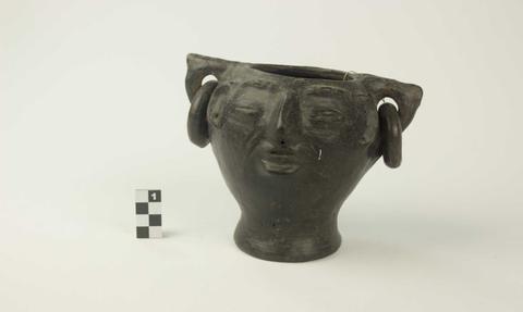 Una jarra de cerámica negra con forma de rostro humano y orejeras.