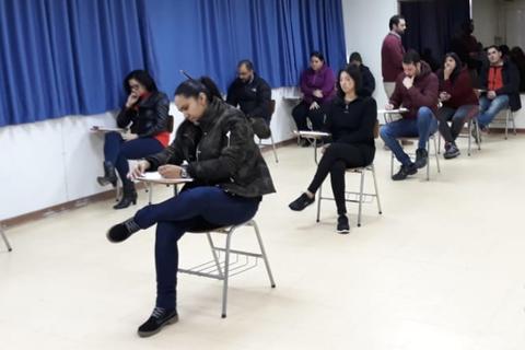 Un grupo de personas sentadas en escritorios en un salón de clases.