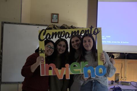 Cuatro amigas sostienen una pancarta que dice 'Campamento de Invierno'.