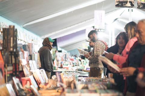 Un grupo de personas explora un mercado lleno de libros y revistas bajo una carpa.