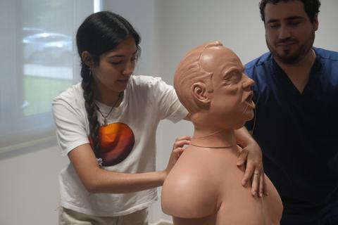 Una mujer está ajustando un maniquí de entrenamiento médico mientras un hombre observa.