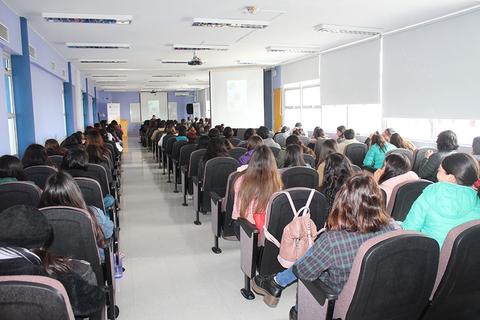 Un aula con muchas personas sentadas en filas, enfocadas en una presentación frente a ellas.