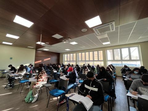 Un grupo de estudiantes está realizando un examen en un aula amplia y luminosa.