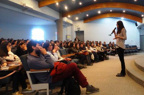 Una oradora presenta frente a un gran público en un auditorio.