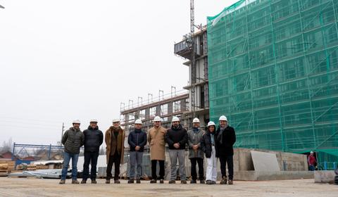 Un grupo de personas está posando frente a un edificio en construcción cubierto con una malla verde.