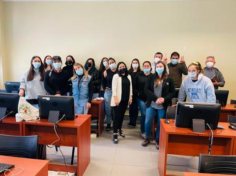 Un grupo de personas sonrientes posando en un aula con computadoras.