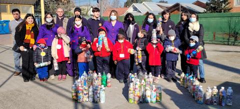 Grupo de personas, incluyendo niños, posando con botellas recicladas en un espacio al aire libre.