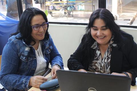 Dos mujeres sonríen mientras trabajan juntas en una computadora portátil.