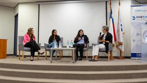 Un grupo de mujeres discutiendo en un panel en una sala con banderas chilenas.