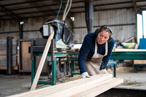 Una mujer trabaja en un taller de madera, utilizando maquinaria para darle forma a los troncos.