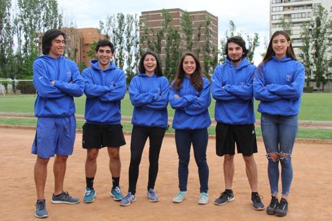 Un grupo de seis jóvenes posa en un campo de deportes, todos vistiendo sudaderas azules.