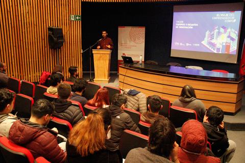 Una conferencia en un auditorio con un ponente frente a un público atento.