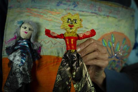 Unas muñecas de tela, una con un diseño colorido y otra con cabello gris, son sostenidas por una mano.