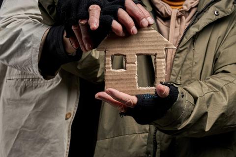 Dos personas sostienen un modelo de casa de cartón entre sus manos.