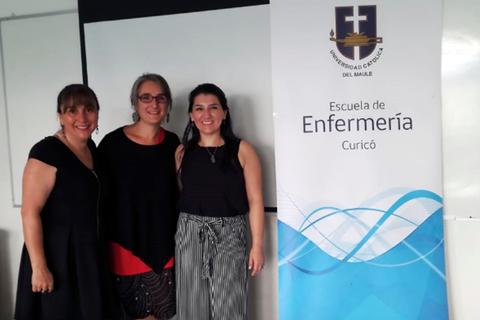 Tres mujeres posan juntas junto a un banner de la Escuela de Enfermería de la Universidad Católica del Maule.