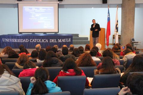 Una conferencia en la Universidad Católica del Maule con un ponente y un público atento.