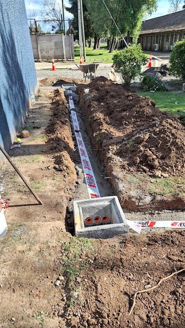 Una zanja excavada en el suelo con tuberías y un pozo de desagüe en construcción.