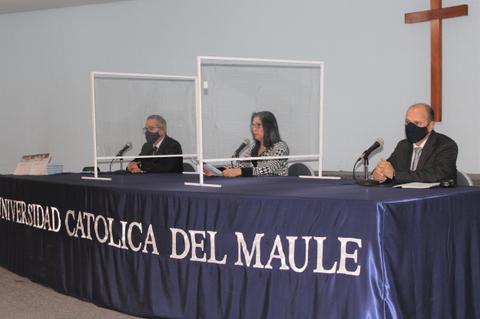 Tres personas sentadas detrás de un escritorio en una universidad, con paneles de protección y usando mascarillas.