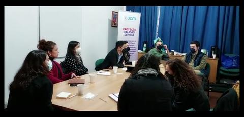Un grupo de personas reunidas en una sala, discutiendo alrededor de una mesa.