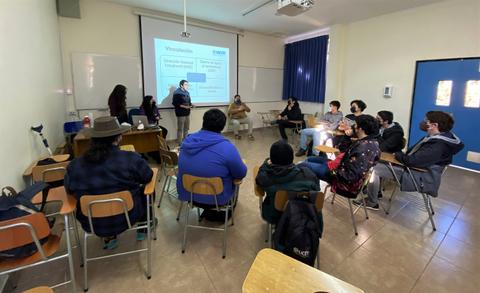 Un grupo de estudiantes participa en una clase en un aula con una presentación proyectada en la pared.