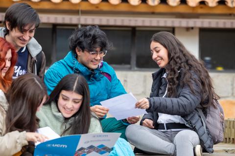 Un grupo de jóvenes se ríe y comparte hojas en un ambiente relajado.
