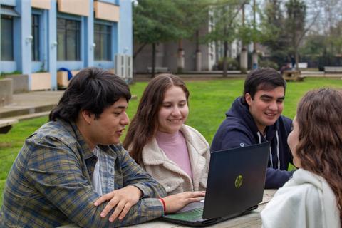 Un grupo de jóvenes se ríe y conversa mientras trabajan en una computadora portátil al aire libre.