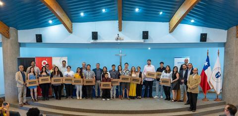 Un grupo de personas sonrientes sosteniendo cajas en un evento en un auditorio.