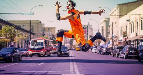 Un hombre disfrazado de payaso salta en una calle urbana.