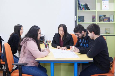 Un grupo de cinco personas trabaja colaborativamente en una mesa en un entorno académico.