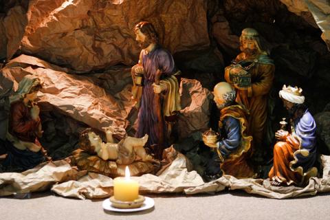 Un nacimiento con figuras de la Virgen María, San José y los Reyes Magos alrededor de una cuna iluminada por una vela.