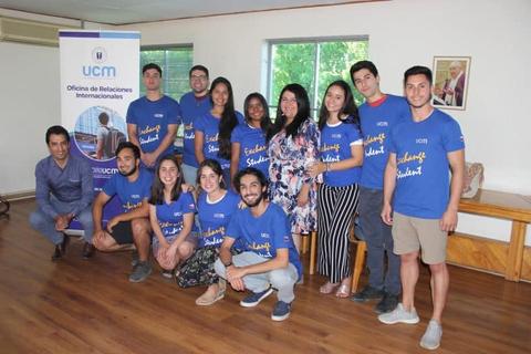 Un grupo de estudiantes posando con camisetas azules frente a un banner de la Oficina de Relaciones Internacionales de UCM.