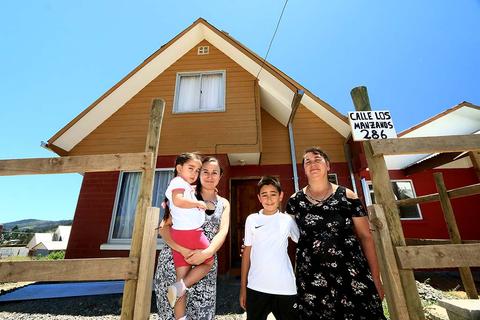 Una familia sonriente posa frente a su casa nueva en un día soleado.