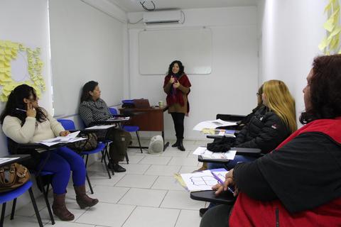 Una reunión en un aula con varias mujeres escuchando a una ponente.