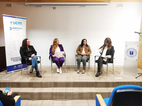 Un panel de discusión con cuatro mujeres sentadas en sillas en un escenario, ante una audiencia durante un evento académico.