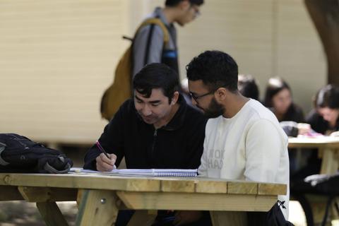 Dos estudiantes están trabajando juntos en una mesa al aire libre.