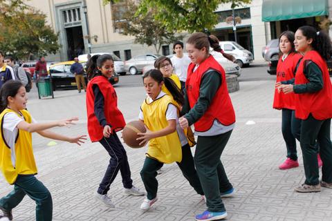 Un grupo de niñas juega al baloncesto en un parque, vestidas con camisetas de colores diferentes.
