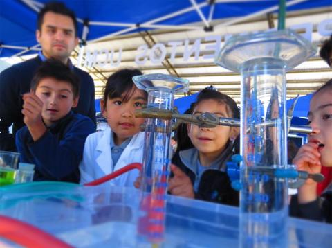Un grupo de niños observa atentamente un experimento de ciencias en un evento educativo.