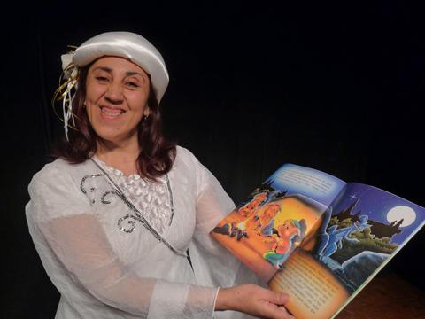 Una mujer sonriente viste de blanco y sostiene un libro ilustrado mientras posa para la foto.