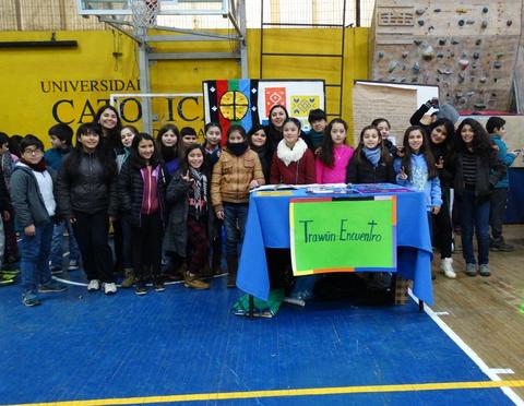 Un grupo de estudiantes sonrientes posando junto a una mesa en un evento escolar.