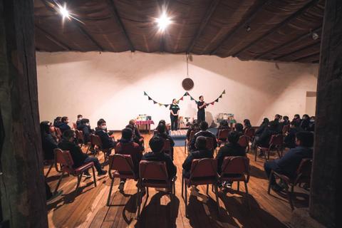 Un grupo de personas observa una presentación en un salón con sillas dispuestas en filas.