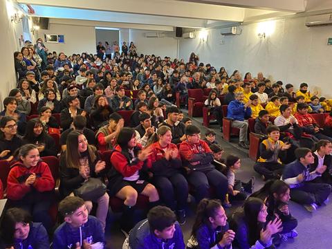 Una multitud de niños y jóvenes aplaudiendo en un evento en un auditorio.