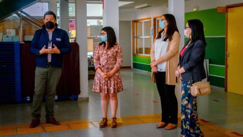 Un grupo de personas con mascarillas conversa en un salón iluminado.