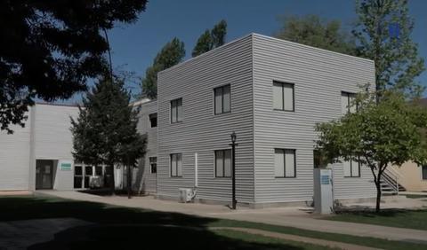 Edificio moderno de estructura metálica con árboles y césped alrededor.