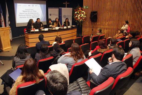 Una conferencia sobre migración en Chile con panelistas y asistentes en un auditorio.
